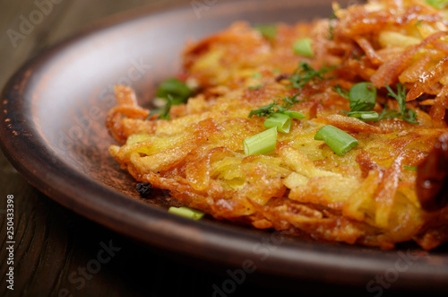 Closeup photo of fresh homemade potato pancakes in clay dish with vegetables