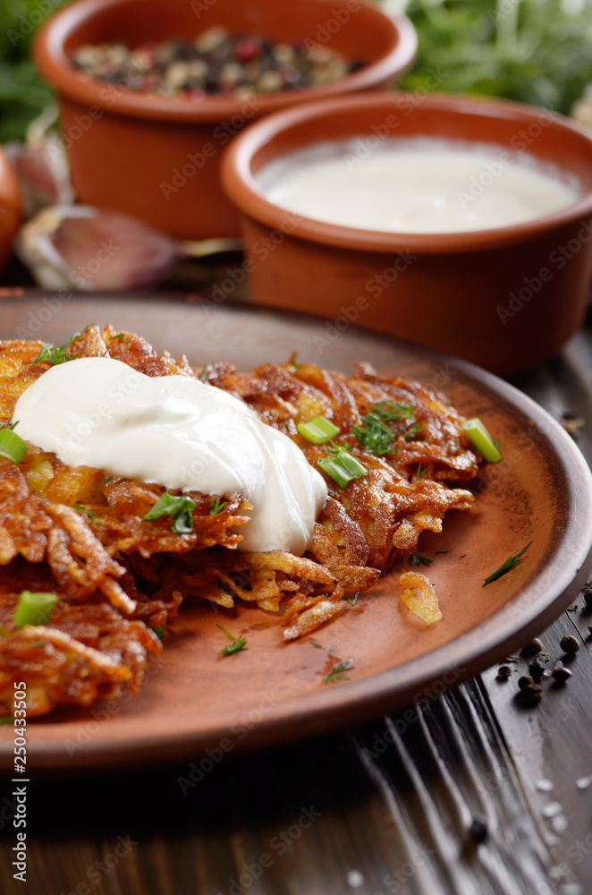 Homemade tasty potato pancakes in clay dish with sun-dried tomatoes and sour cream Homemade tasty potato pancakes in clay dish with sun-dried tomatoes and sour cream