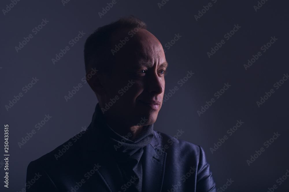 Fototapeta premium Model tests for men. Portrait of an adult male in a low key. Confident look with a smile and a smirk. Blue eyes. Color correction in purple-blue. Stylish image of an adult man