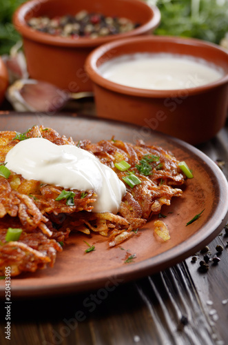 Homemade tasty potato pancakes in clay dish with sun-dried tomatoes and sour cream