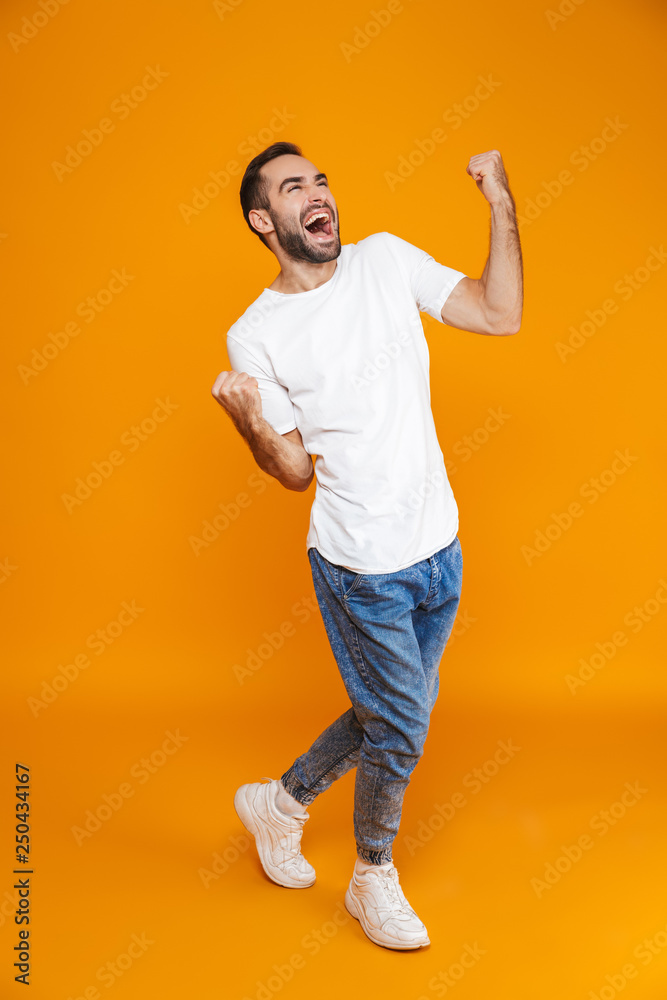 Full length image of good-looking guy 30s in t-shirt and jeans clenching fists while standing, isolated over yellow background Full length image of good-looking guy 30s in t-shirt and jeans clenching fists while standing, isolated over yellow background