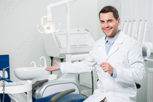 handsome dentist smiling while gesturing in clinic