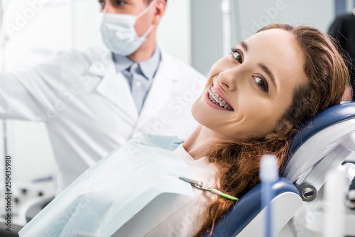 selective focus of beautiful woman in braces during examination of teeth near dentist photo