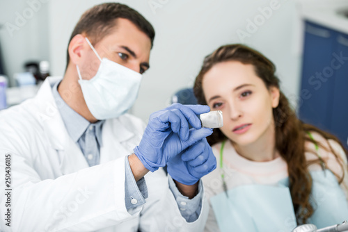 selective focus of x-ray of teeth in hands of dentist in latex gloves and mask near patient