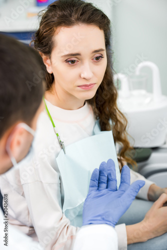 selective focus of pensive woman near dentist wearing latex gloves