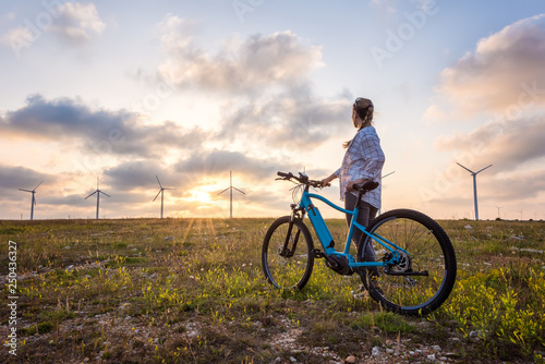 Woman with a bike in the nature / A woman with a bike enjoys the view of sunset over a summer field with a wind farm