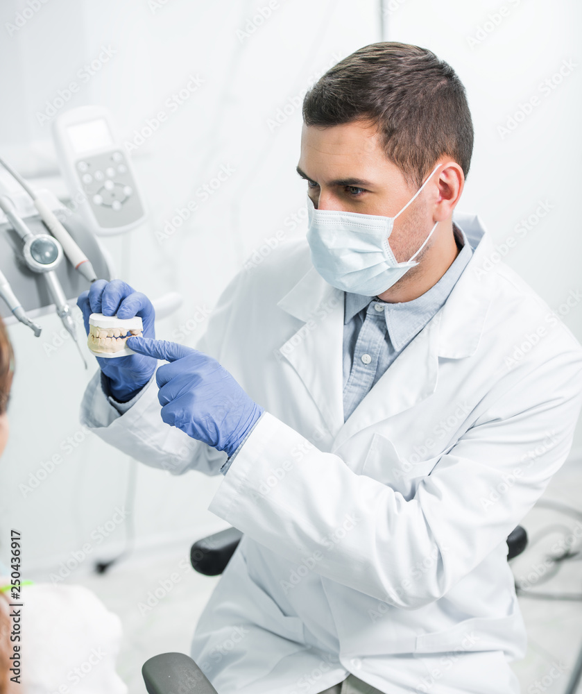 dentist in mask and latex gloves pointing with finger at teeth model near female patient dentist in mask and latex gloves pointing with finger at teeth model near female patient