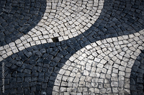 Shapes and patterns of a cobbled street of Lisbon (Portugal). Rounded and waving black and white shapes with an empty cobblestone space