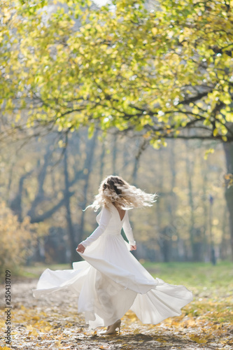 Look from behind at charming bride whirling in autumn park covered with fallen leaves