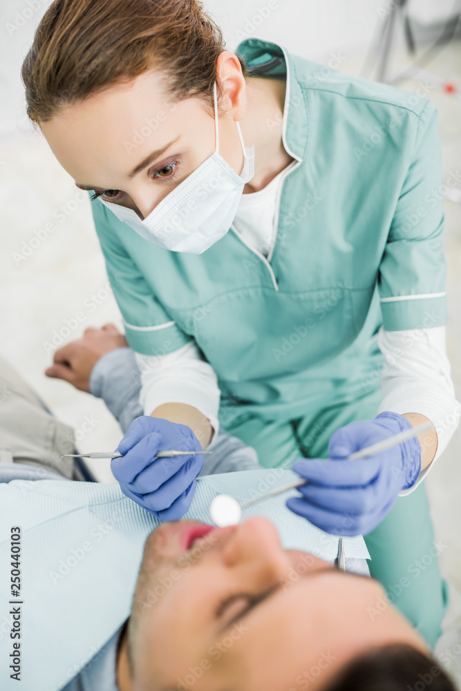 selective focus of female dentist in mask holding dental instruments and examining patient selective focus of female dentist in mask holding dental instruments and examining patient