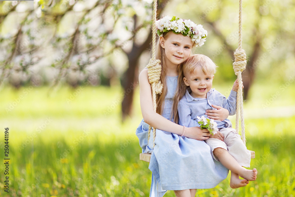 Cute girl and boy having fun on a swing in blossoming old apple tree garden. Sunny day. Spring outdoor activities for kids Cute girl and boy having fun on a swing in blossoming old apple tree garden. Sunny day. Spring outdoor activities for kids