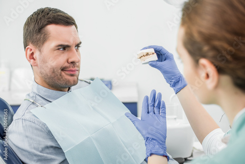 selective focus of confused man looking at teeth model in hand of female dentist