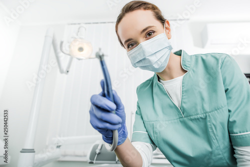 selective focus of dentist in mask and latex gloves holding dental drill