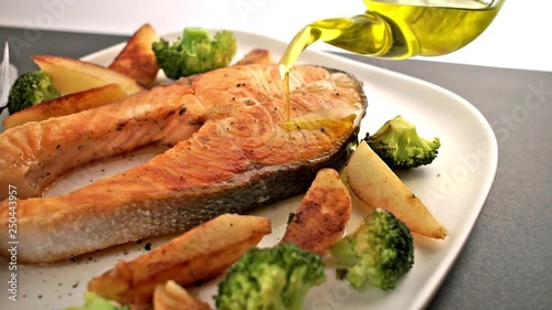 Meal with salmon fish steak and vegetable. Bottle of Olive oil pouring on salmon fish. Healthy food. Main course Close up. Slow motion video footage. Slowmo. Slow-mo photo