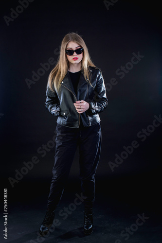 young girl in a black leather jacket and sunglasses on a dark background standing