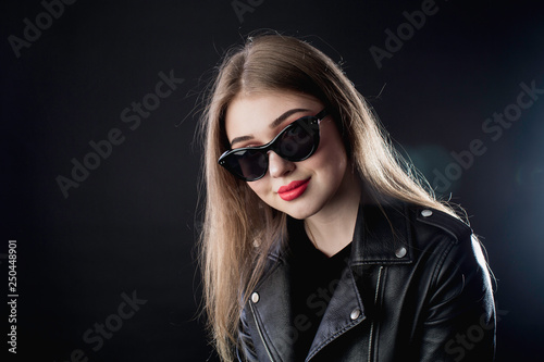 portrait of a young girl in a black leather jacket and sunglasses on a dark background in the studio