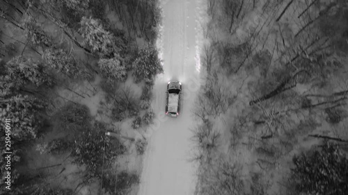 Tracking birdseye drone shot of SUV on snow covered rural road. Evening drive with headlights on, in Northern Ontario, Canada. Winter driving. Black and white except for red taillights. photo