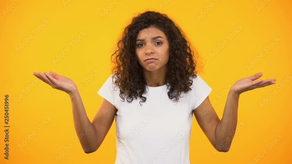 Afro-american female shrugging shoulders, unsure of choice, yellow background Afro-american female shrugging shoulders, unsure of choice, yellow background