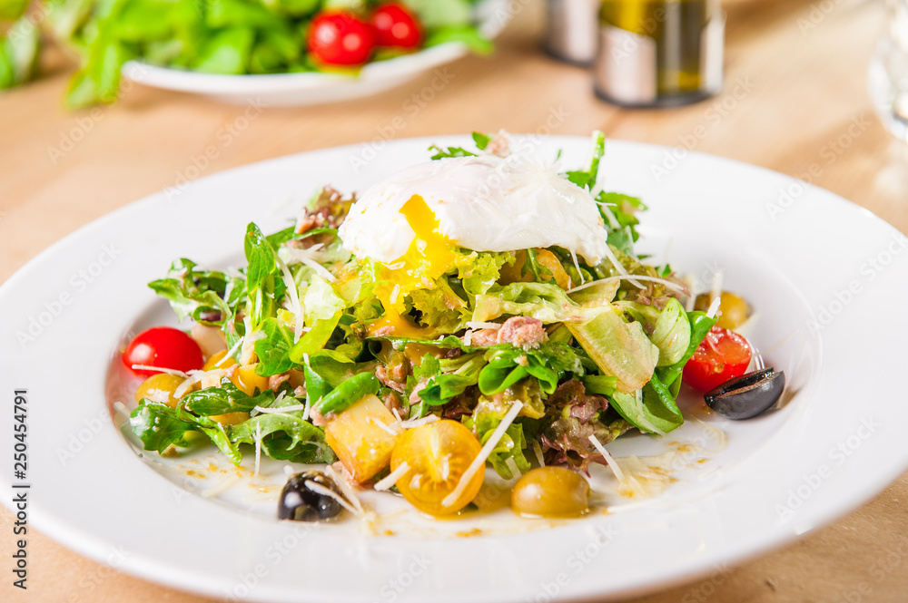 Close up Green Vegetable Salad with tuna and Poached Egg on the white plate on the wooden served table. Selective focus, copy space.