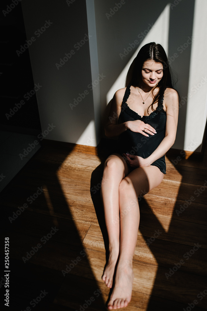 Fototapeta premium Waiting baby. Pregnant woman sitting near window and hands embraces a round belly, stomach. close-up. nine months. Baby Shower. Motherhood concept. front view.