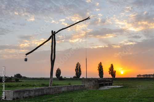 Traditional water well (well sweep or shadoof) in Serbia with a beautifull sunset photo