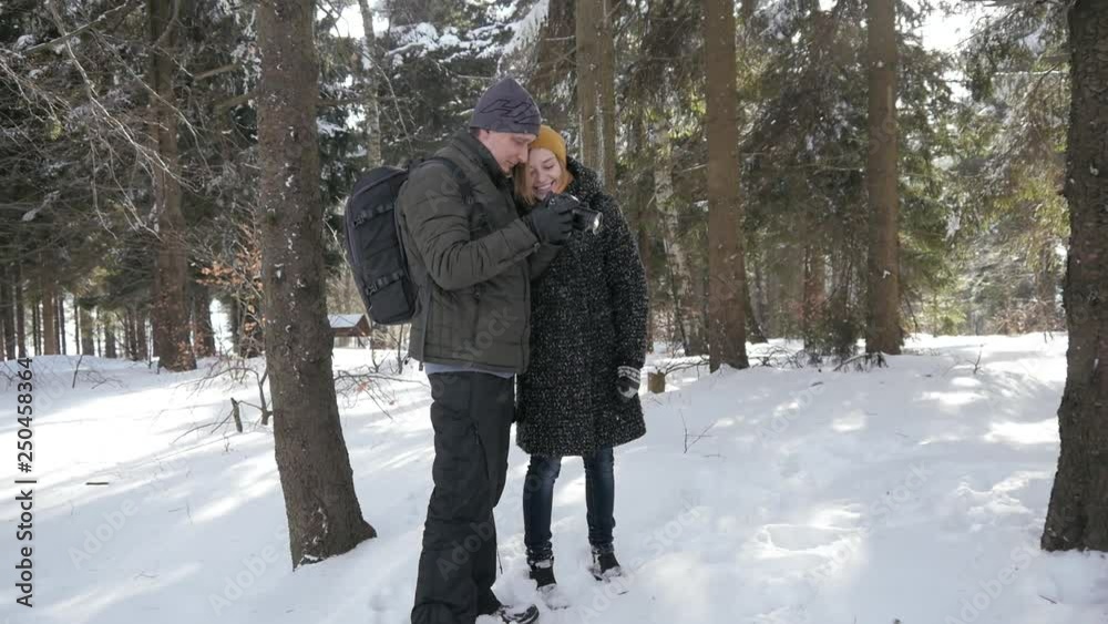 Man and Woman Tourists watch Photos on a Photo Camera through the Winter Forest Man and Woman Tourists watch Photos on a Photo Camera through the Winter Forest