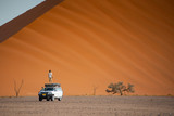Two Asian man traveler and photographer standing and sitting on camper car near orange sand dune. Travel desert concept