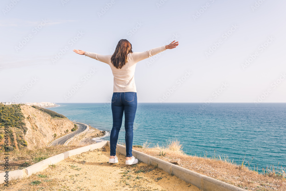 young woman with open arms looking at the sea