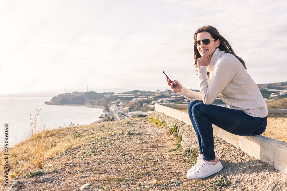 young woman using her mobile phone in front of the sea in spring