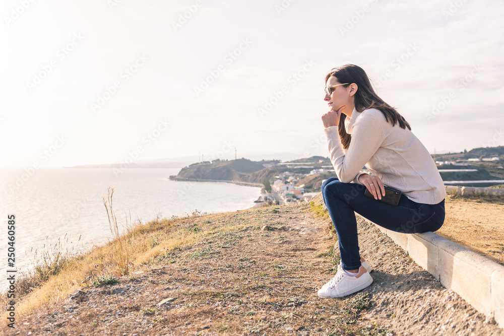 young woman sitting watching the sunset in front of the sea