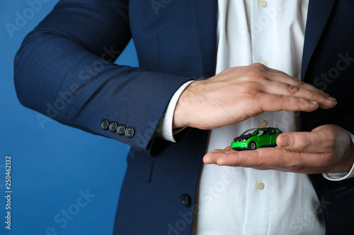 Insurance agent holding toy car on color background, closeup