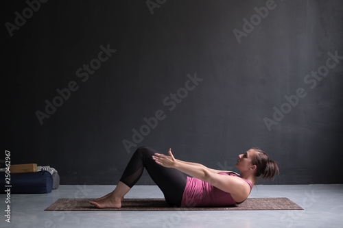 Young woman practicing yoga asana Ardha Navasana exercise at the yoga studio