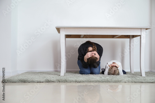 Obraz na plátně Mother with daughter under table during earthquake indoors