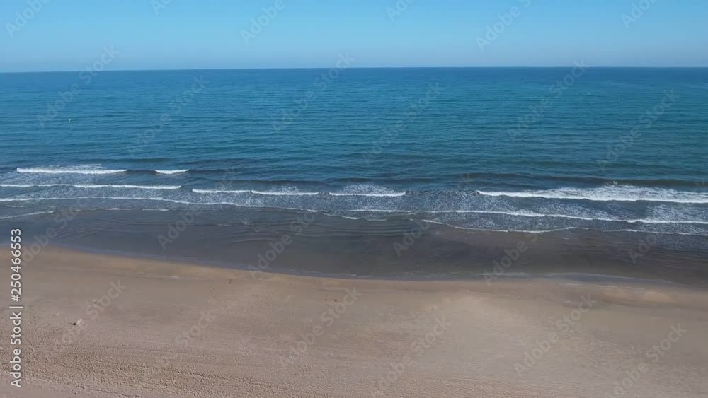 The drone flies along the seashore and removes the waves hitting the coastal sand. Clear sky, clean sand. The drone flies along the seashore and removes the waves hitting the coastal sand. Clear sky, clean sand.