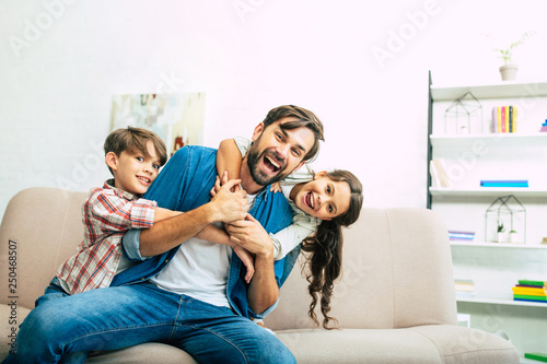 We are loving our father very much. Handsome dad playing with beautiful happy kids on the couch at home photo