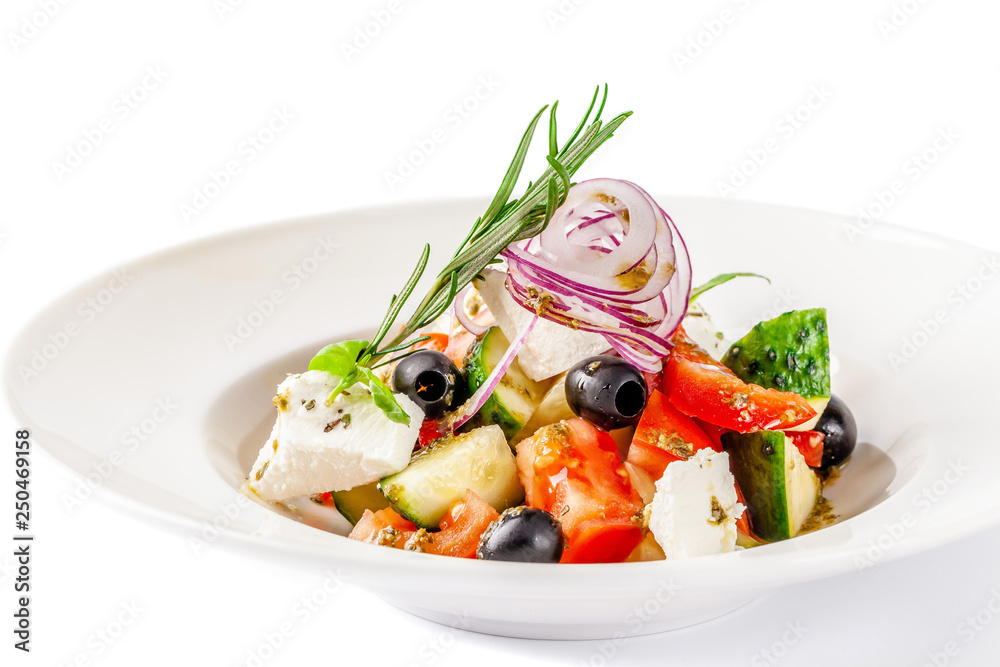 Concept of Greek cuisine. Salad of tomato, cucumber, bell pepper, olives and feta cheese. dressed with olive oil and decorated with fresh basil. White plate on a white background.