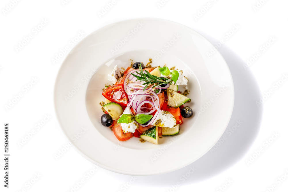 Concept of Greek cuisine. Salad of tomato, cucumber, bell pepper, olives and feta cheese. dressed with olive oil and decorated with fresh basil. White plate on a white background.