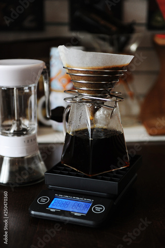Alternative manual coffee brewing with paper filter in stainless steel dripper. On the electronic scale. Manual grinder