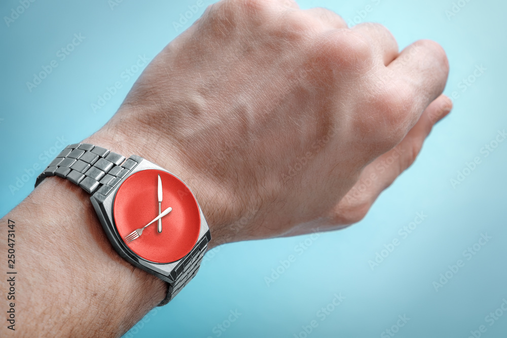 Fototapeta premium Wrist watch on man's hand. Plate, knife and fork on clock face. Concept of intermittent fasting, lunchtime