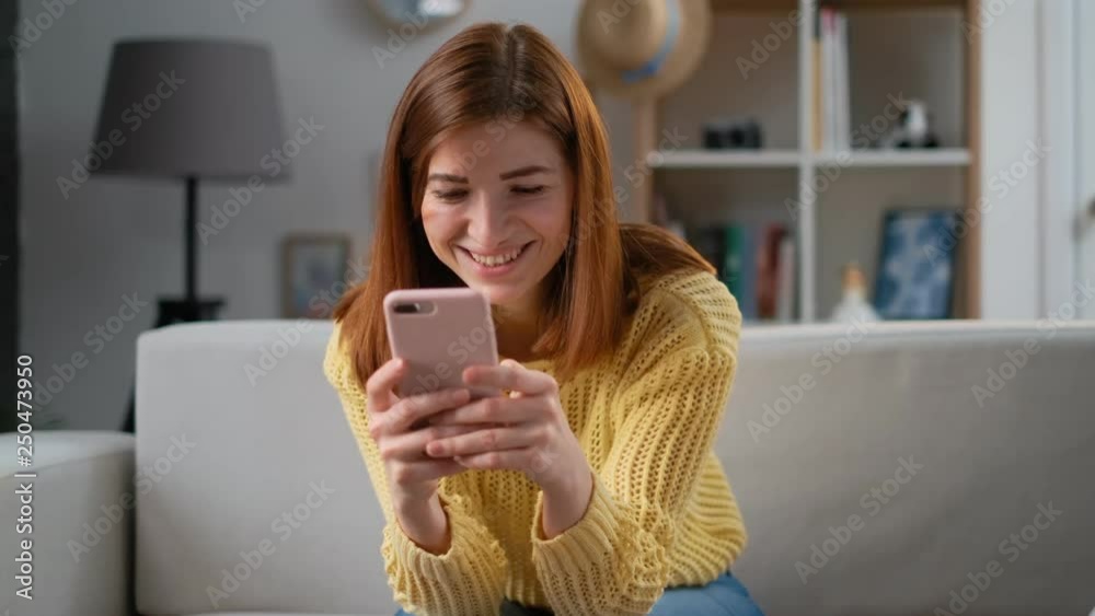 Young successful woman using smartphone app at home living room home. Excited girl receiving good news excited happy cheerful smiling. Success and achievement concept Young successful woman using smartphone app at home living room home. Excited girl receiving good news excited happy cheerful smiling. Success and achievement concept
