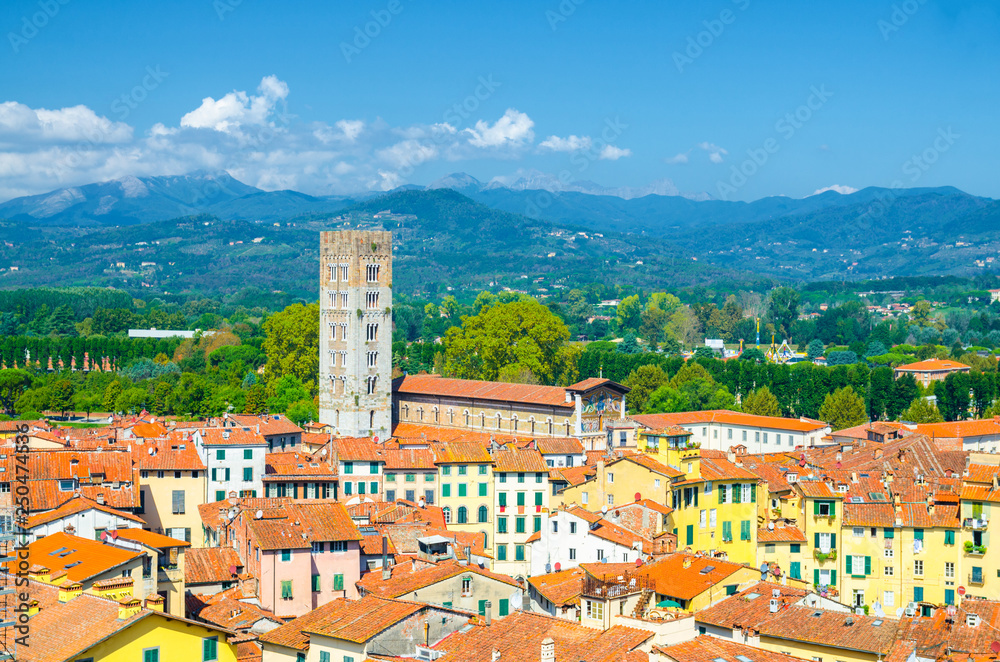 Aerial top panoramic view of Chiesa di San Frediano catholic church bell tower in historical centre medieval town Lucca with terracotta tiled roofs and green hills background, Tuscany, Italy