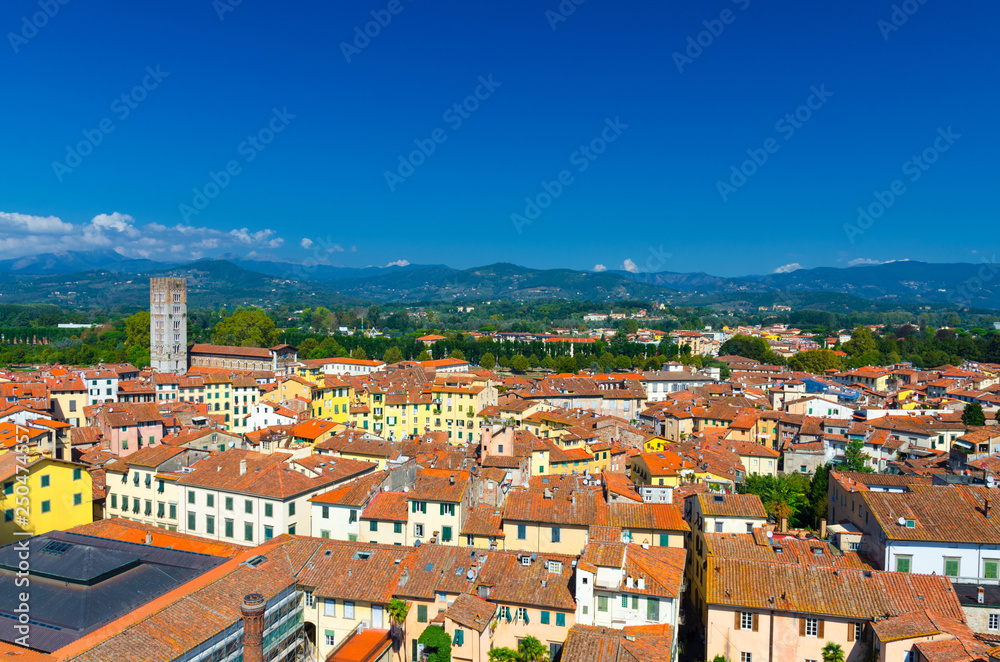 Aerial top panoramic view of Piazza dell Anfiteatro square, Chiesa di San Frediano church in historical centre medieval town Lucca with terracotta tiled roofs, green hills background, Tuscany, Italy
