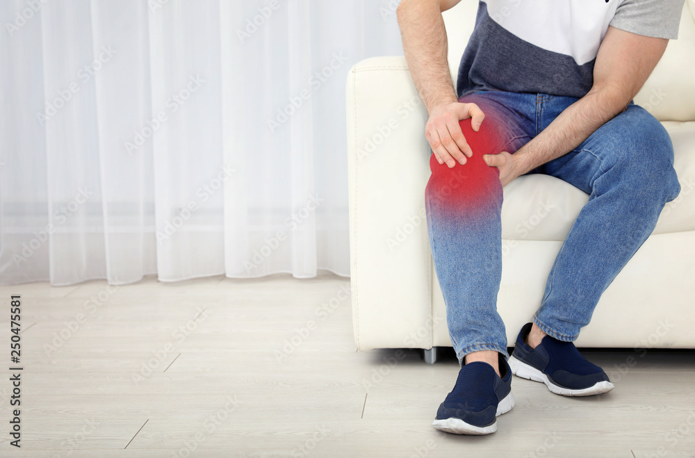 Man suffering from leg pain indoors, space for text Man suffering from leg pain indoors, space for text