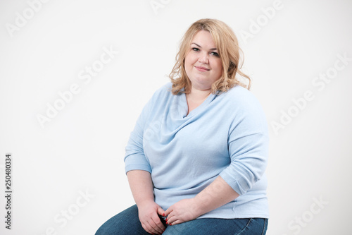 Young obese woman in casual blue clothes on a white background in the studio. Bodypositive.