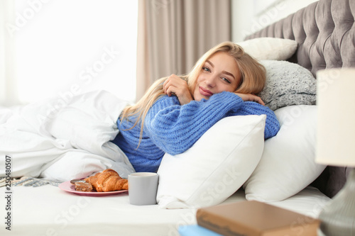 Beautiful young woman lying with breakfast in bed at home. Winter atmosphere