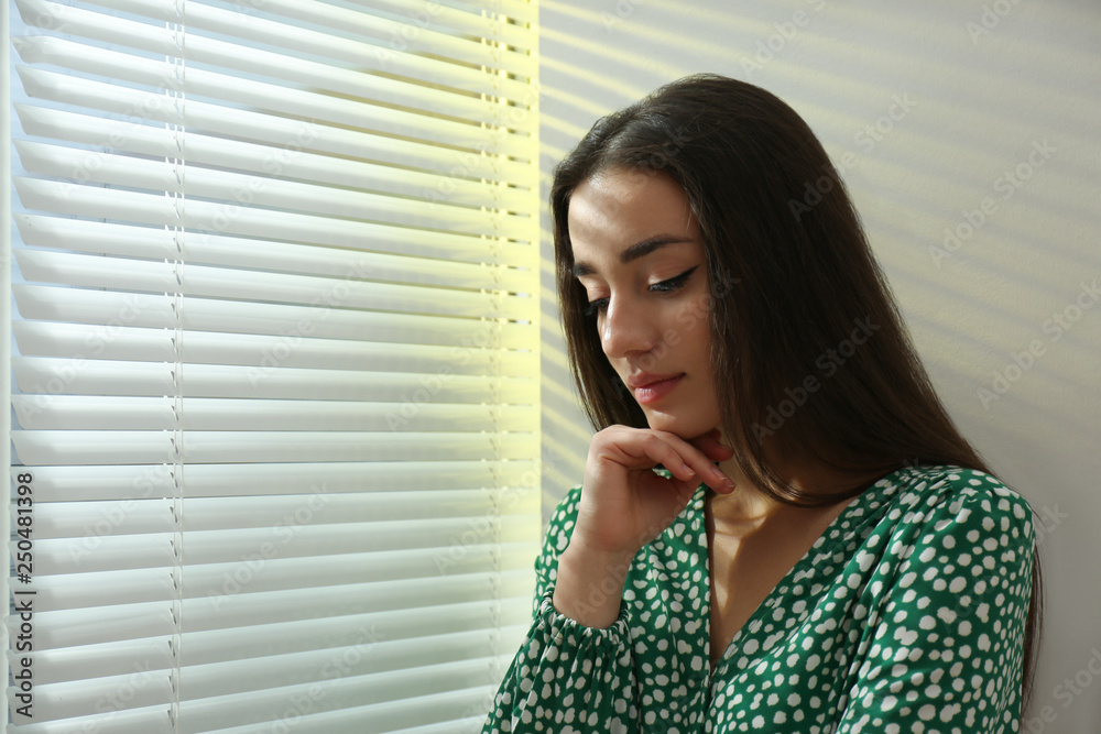 Young woman near window with Venetian blinds. Space for text Young woman near window with Venetian blinds. Space for text