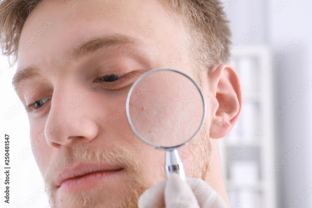 Dermatologist examining patient with magnifying glass in clinic, closeup view Dermatologist examining patient with magnifying glass in clinic, closeup view