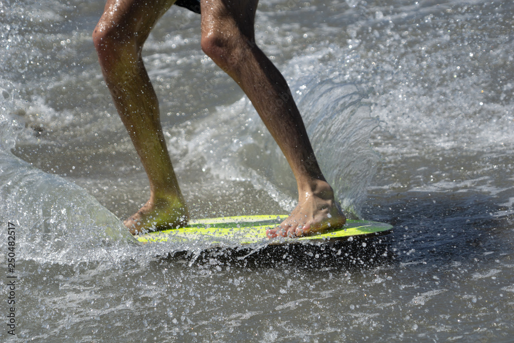 Skim-boarding on yellow board in shallow water.