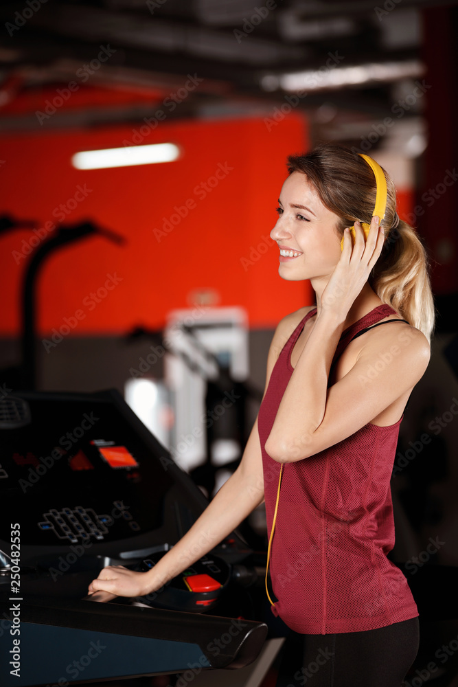 Fototapeta premium Young woman listening to music with headphones at gym