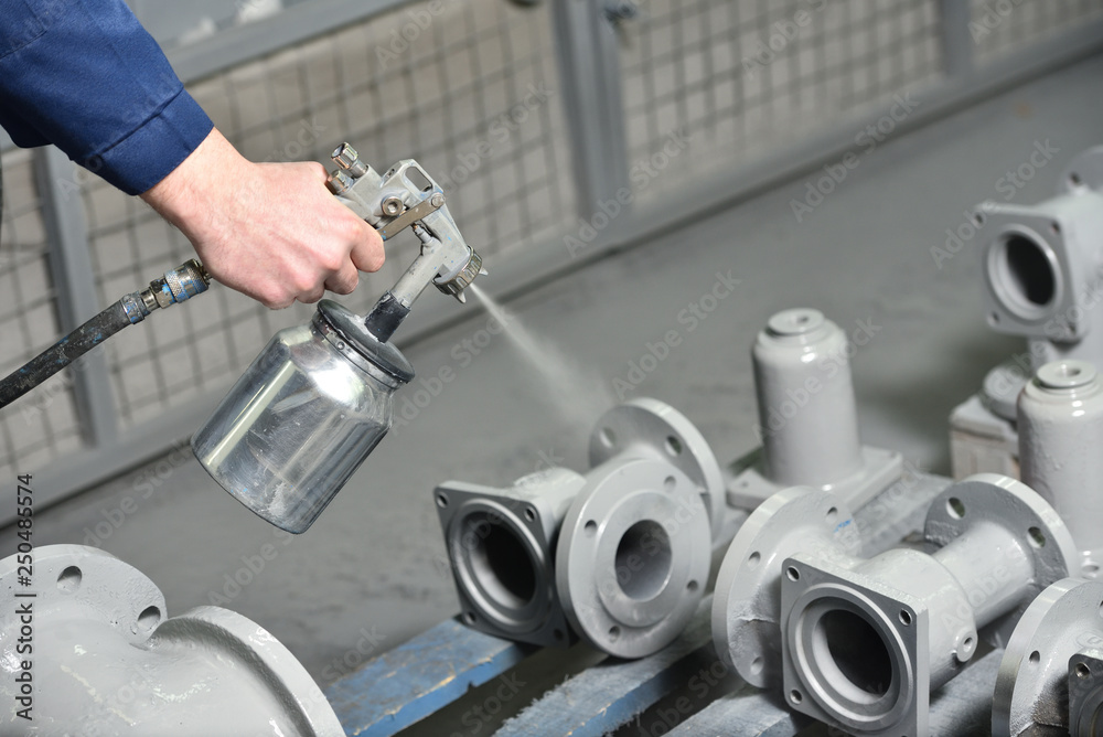A worker at a factory in a special room paints parts of the valves from